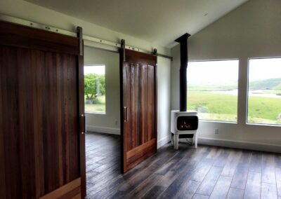 A cozy room featuring a wood-burning stove and sliding barn doors with a view of a green landscape outside.