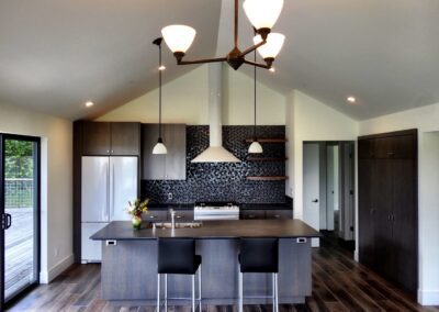 Modern kitchen interior with dark cabinets, stainless steel appliances, a central island with bar stools, and pendant lighting.