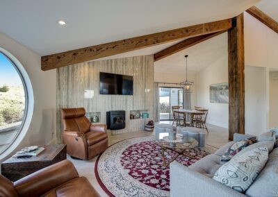 Modern living room interior with rustic elements, featuring leather chairs, a circular window, exposed wooden beams, and a mounted television.