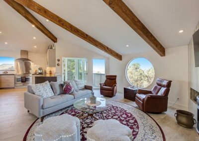 A bright, modern living room with exposed wooden beams, large windows, and a mix of contemporary and classic furnishings.