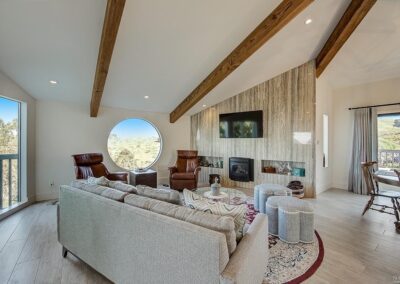 Bright living room with vaulted ceiling featuring exposed wooden beams, a mounted tv, and a comfortable seating area that opens to a scenic outdoor view.