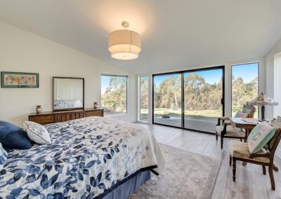 Bright bedroom with a floral-patterned bedspread, sliding glass doors, and a view of trees.