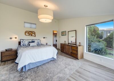 A bright and neatly arranged bedroom with a large bed, wooden furniture, and a view of the garden through a window.