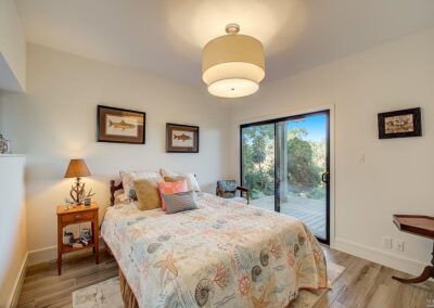 Modern bedroom with a marine-themed bedspread, wooden flooring, and sliding glass door leading to an outdoor area.